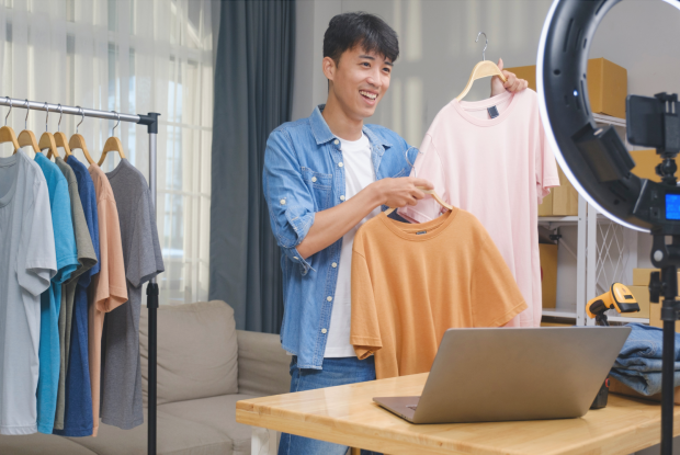 Ein junger Mann hält seine T-Shirts in die Kamera und lächelt