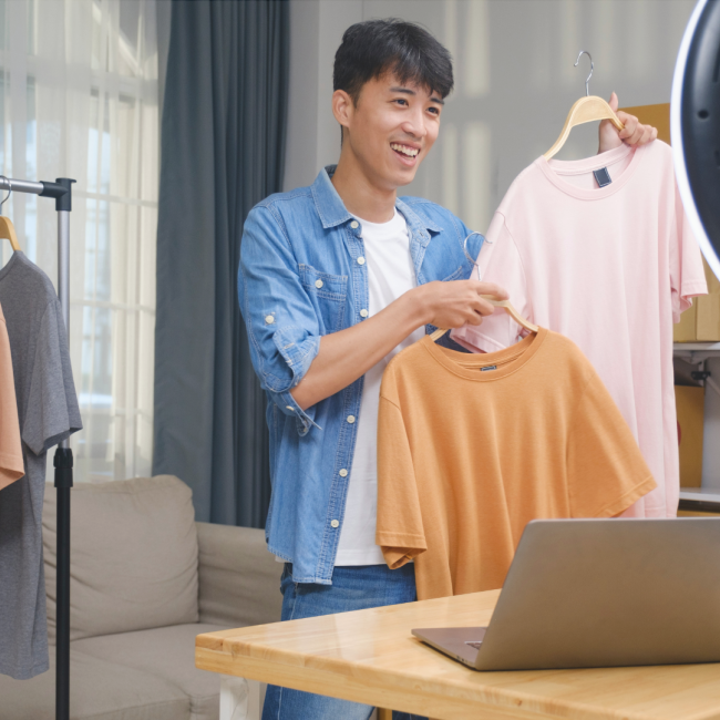 Ein junger Mann hält seine T-Shirts in die Kamera und lächelt